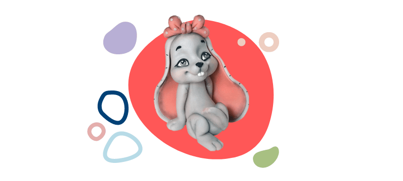 A cute cartoon rabbit with big ears and a pink bow on its head sits in front of a red circular background, surrounded by colorful abstract shapes. Perfect as a fondant cake topper, check out the video tutorial to create your own.