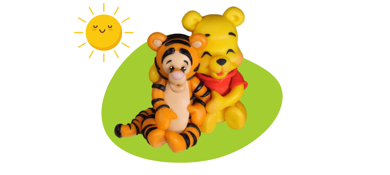 Two cartoon characters, resembling Baby Winnie The Pooh in a red shirt and Baby Tigger with orange stripes, share a hug under the sun. Their adorable figures could easily be mistaken for fondant cake toppers due to their charming details.